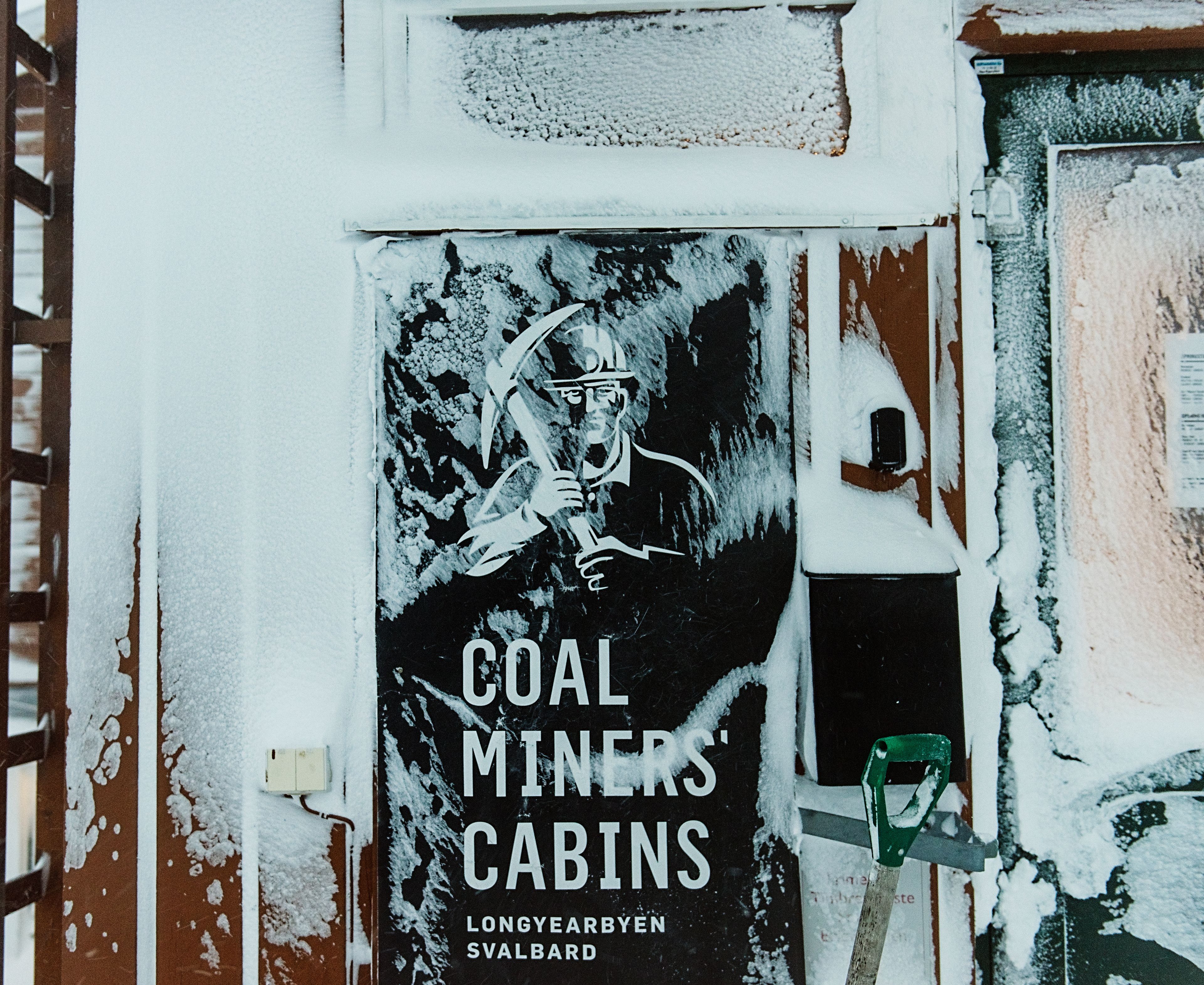 Un edificio con un cartel que dice 'Coal Miners' Cabins' y una pala verde apoyada en la pared.