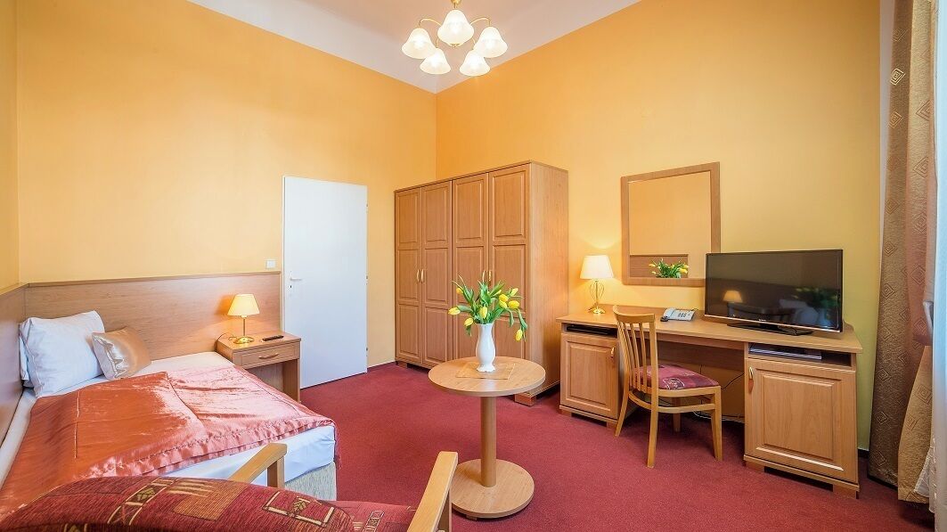 Habitación de hotel con cama, escritorio, silla, televisor y armario.