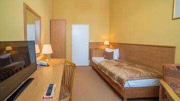 A hotel room with a bed, a desk with a TV, a chair, a lamp, and a bedside table.