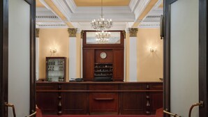 A reception area with a red carpet, wooden reception desk, a clock, and a chandelier. - Spa Hotel Savoy (Frantiskovy Lazne)