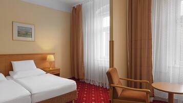 Una habitación de hotel con una cama, una silla, una mesa, una lámpara y una ventana con cortinas.