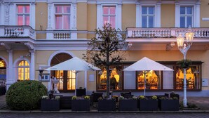 A building with ornate architecture, outdoor seating with umbrellas, and a well-maintained garden. - Spa Hotel Savoy (Frantiskovy Lazne)