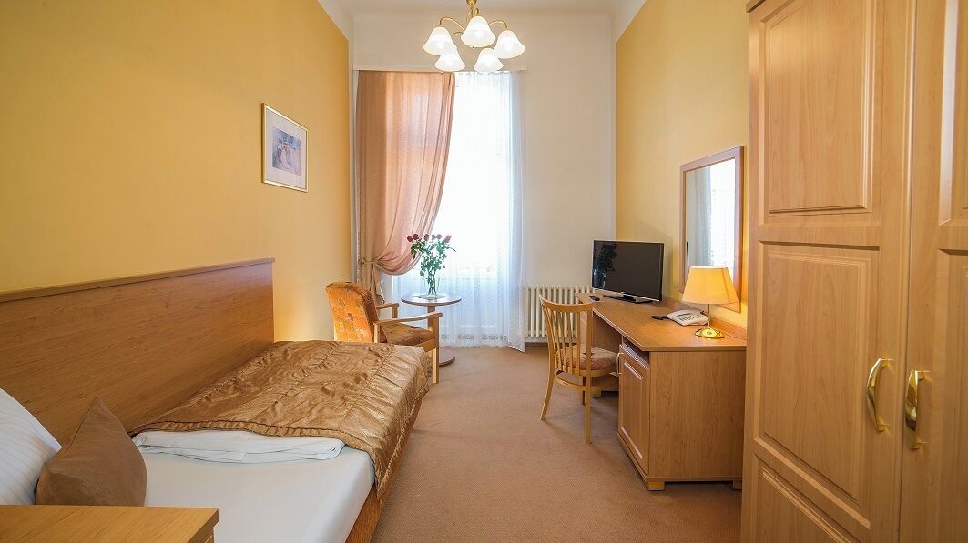 Habitación de hotel con cama, escritorio con computadora, silla, una mesita con un florero y armario.