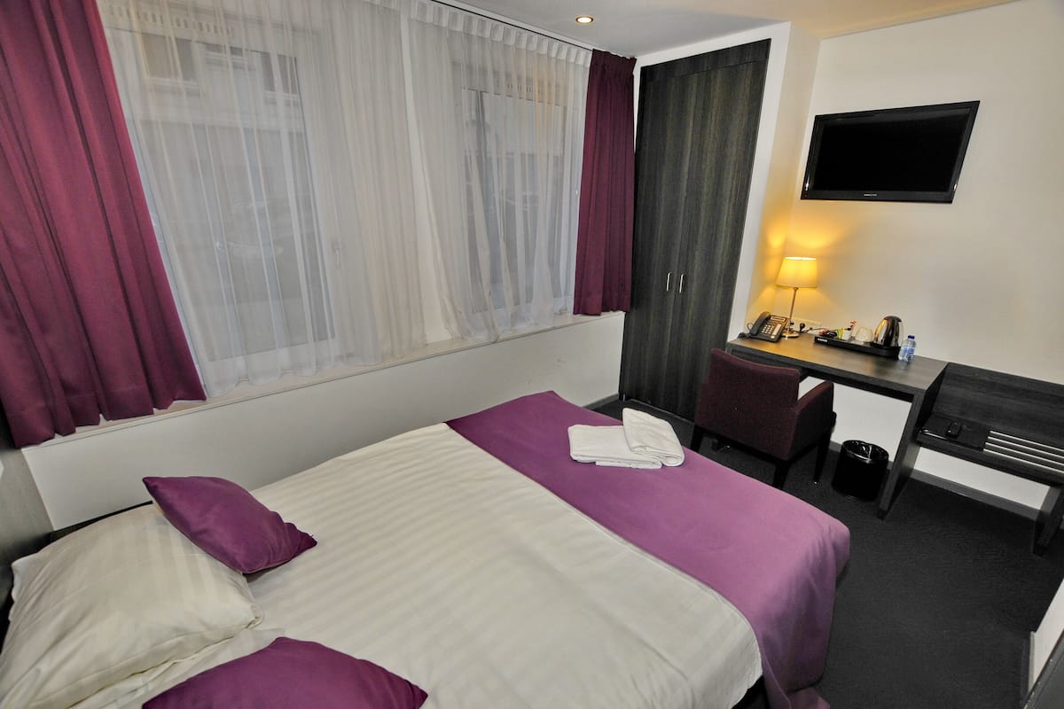 A hotel room with a bed, a desk with a chair, a TV, and a lamp.
