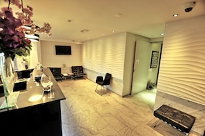 A modern reception area with a marble floor, black chairs, a reception desk, and a wall-mounted TV. - Hotel Park View Amsterdam (Amsterdam)