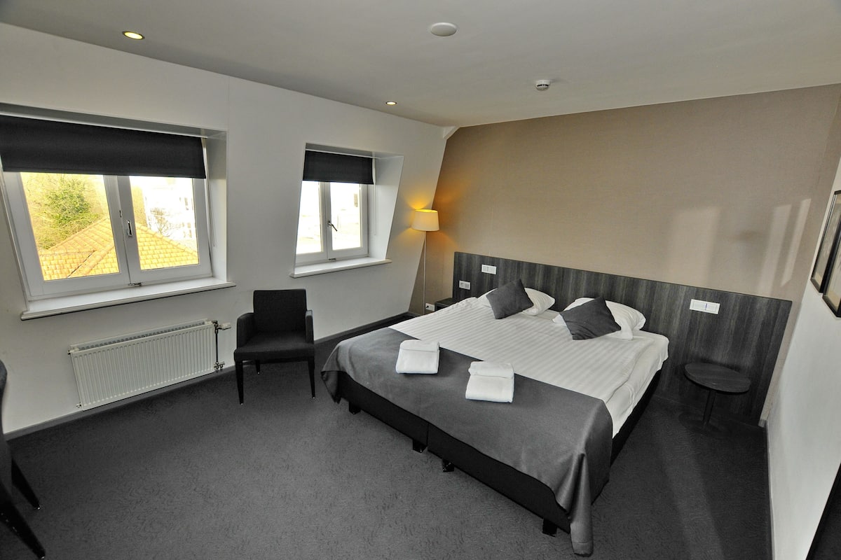 A hotel room with a large bed, a chair, a desk, and a window with a view of the outside.