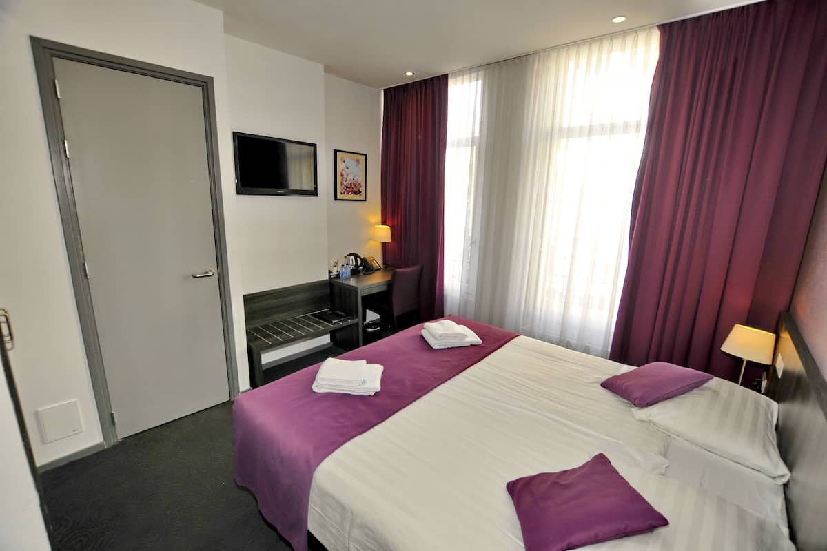 A hotel room with a bed, a desk, a chair, a TV, and a window with curtains.