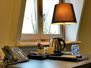 A hotel room desk with a telephone, a remote control, a lamp, a kettle, and bottled water. - Hotel Park View Amsterdam (Amsterdam)