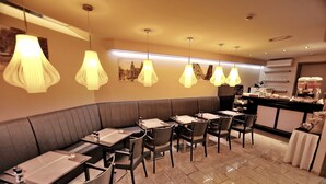 Un restaurante con varias mesas y sillas, una barra con una máquina de café y lámparas colgantes.