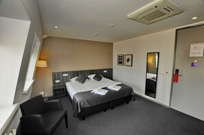 A hotel room with a large bed, a bedside table, a chair, a desk, a lamp, a mirror, and a door with a lock. - Hotel Park View Amsterdam (Amsterdam)