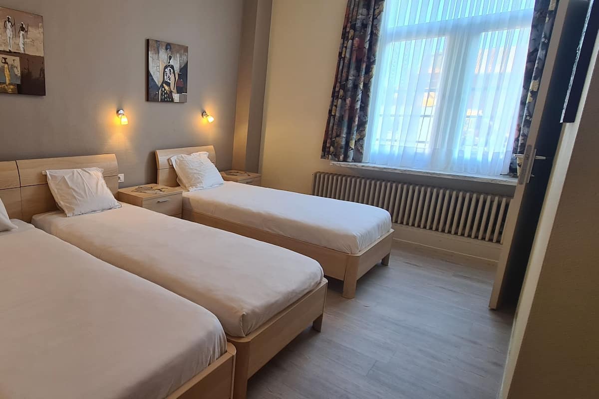 Une chambre d’hôtel avec deux lits simples, des tables de chevet, des œuvres d’art accrochées au mur et une fenêtre avec des rideaux.