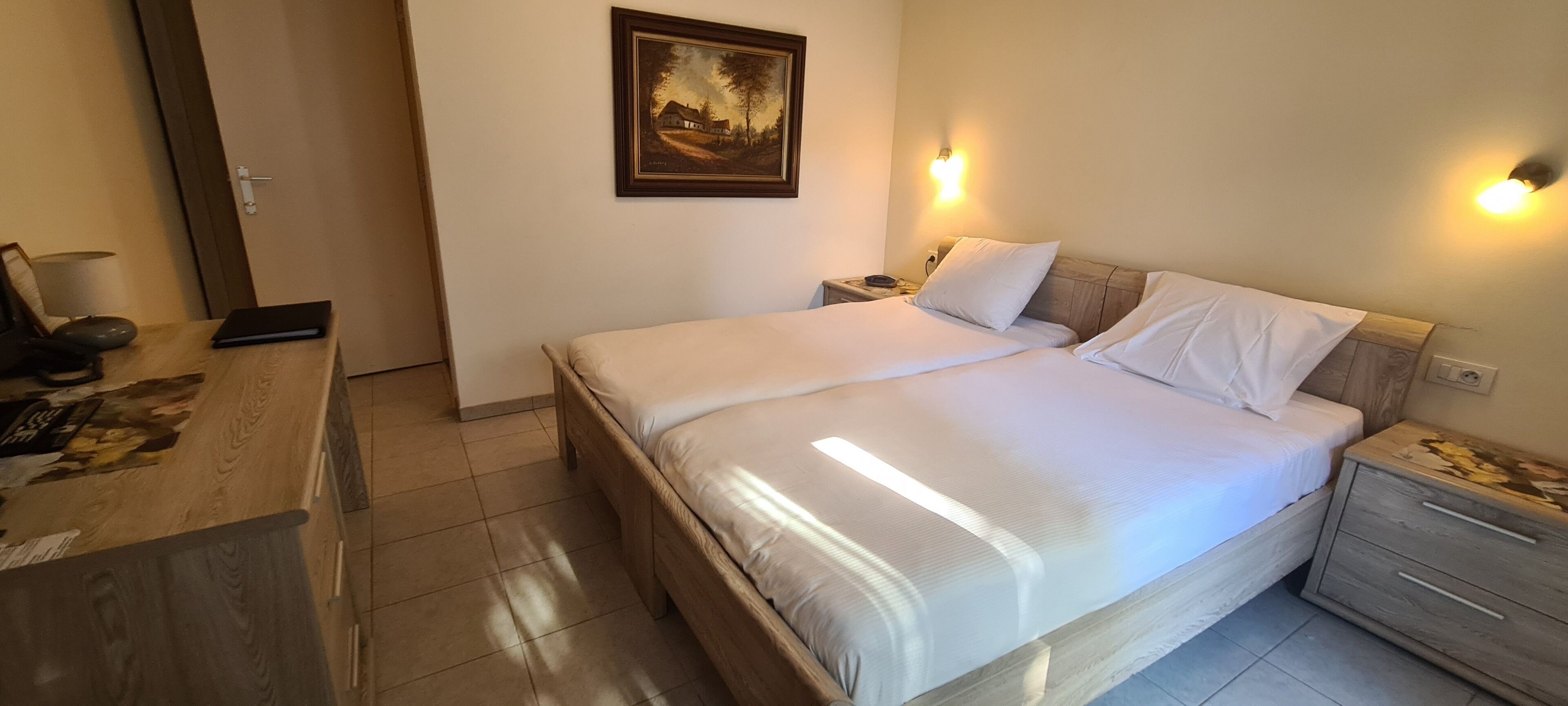 A double bed with white linens, a bedside table with a lamp, and a painting on the wall.
