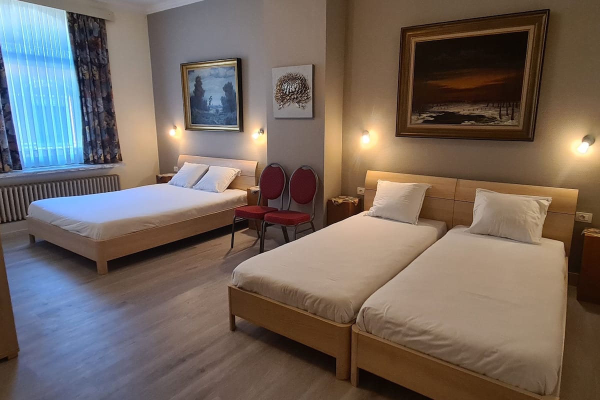 Une chambre d’hôtel avec deux lits simples, une chaise, un radiateur et des œuvres d’art accrochées aux murs.
