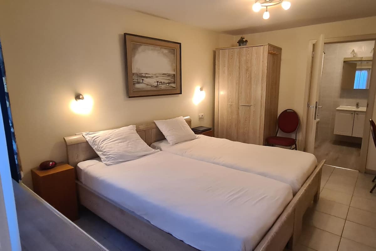 Une chambre d’hôtel avec un grand lit, une armoire, un bureau avec une télévision et une salle de bain visible à travers une porte ouverte.