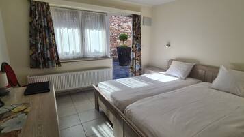 Une chambre d’hôtel avec un lit, un bureau avec un ordinateur, un radiateur et une fenêtre avec des rideaux.