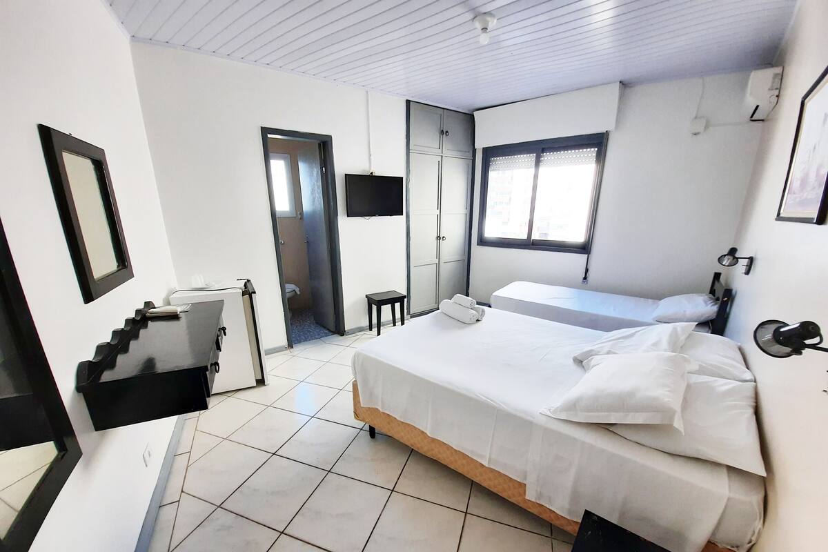 A hotel room with a large bed, a desk, a chair, a small table, a TV, and a window.