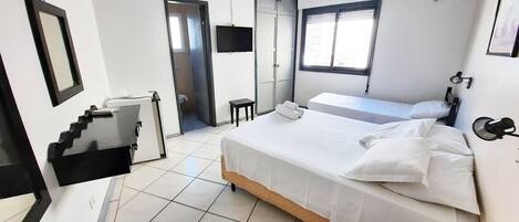 A hotel room with a large bed, a desk, a chair, a small table, a TV, and a window.