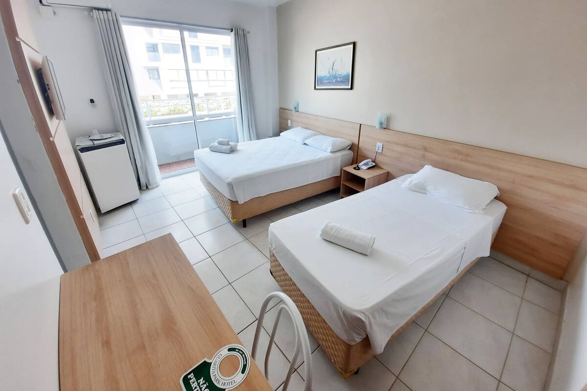 A hotel room with two beds, a desk, a chair, a small fridge, a phone on the nightstand, and a window with curtains.