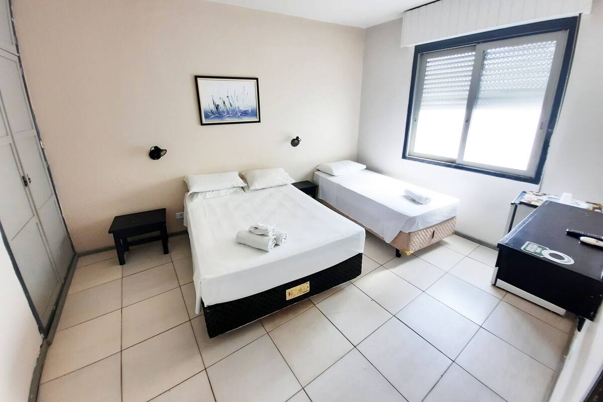 A hotel room with a large bed, a smaller bed, a desk, and a window.