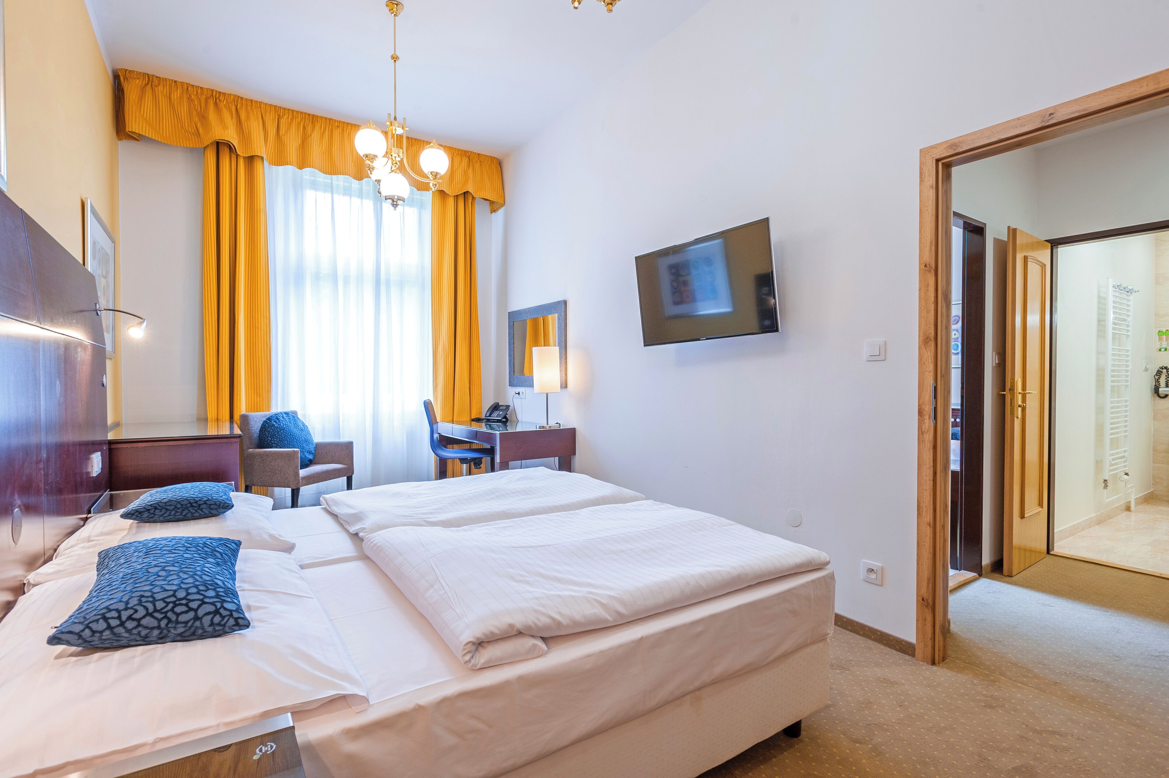 A hotel room with a bed, a desk, a chair, a TV, and a wardrobe.