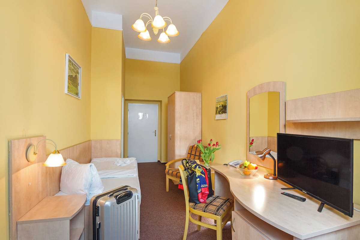 A hotel room with a bed, a desk with a TV, a chair, a lamp, and a suitcase.