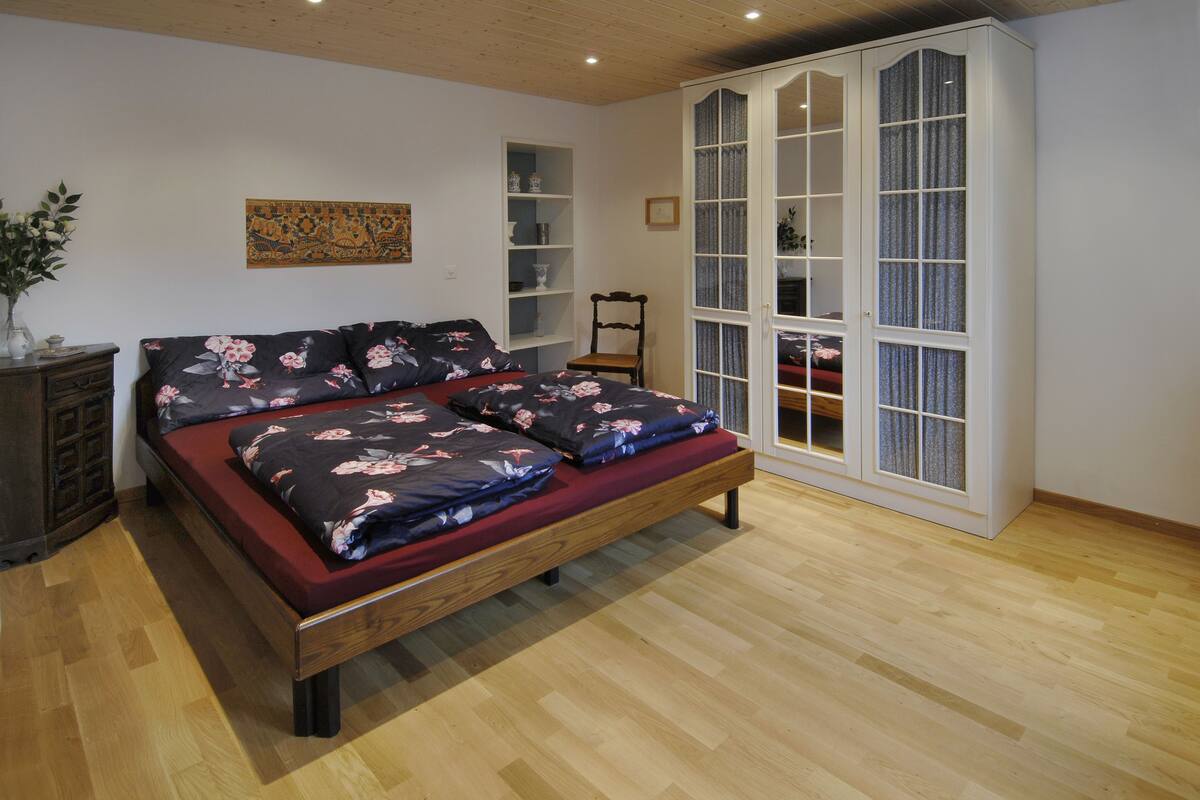 Un dormitorio con una cama de madera, un armario, una mesita y una planta decorativa.