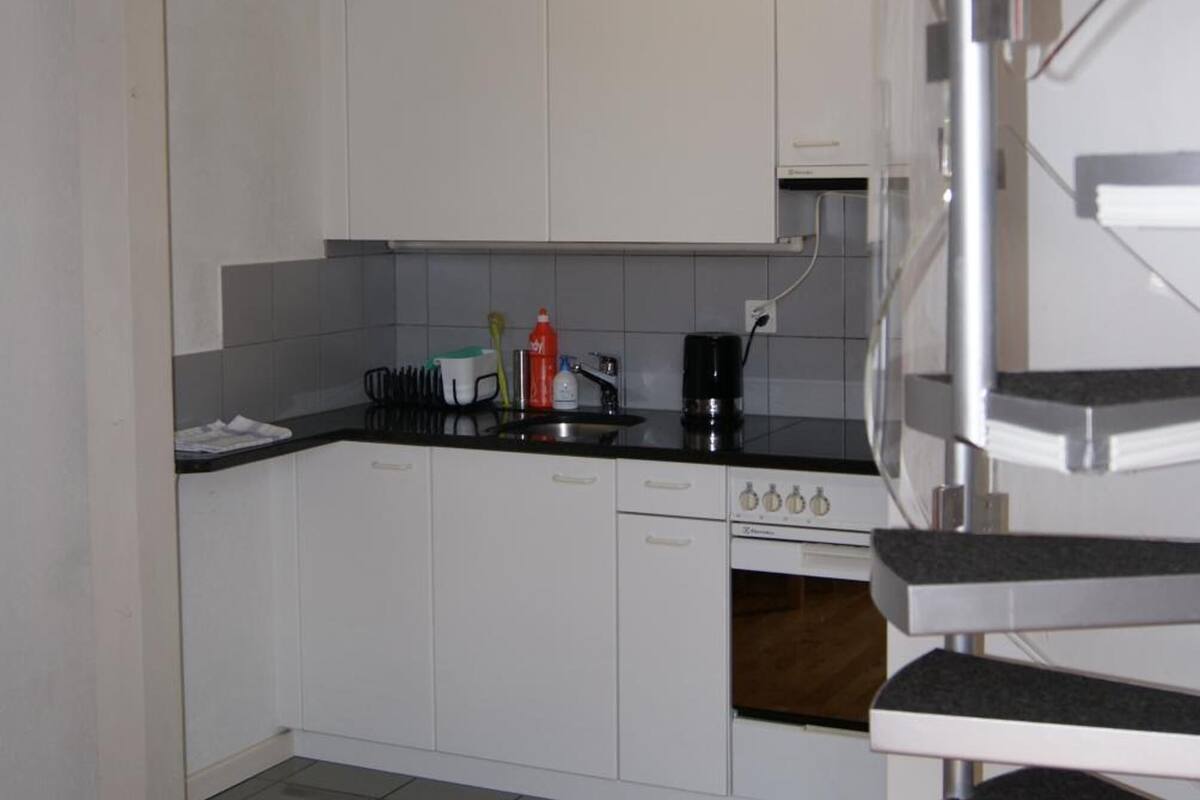 Una cocina moderna con armarios blancos, encimera negra y campana extractora de acero inoxidable.