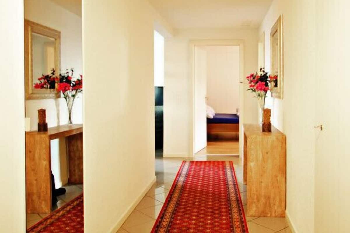Un pasillo con alfombra roja estampada, muebles de madera y adornos florales.