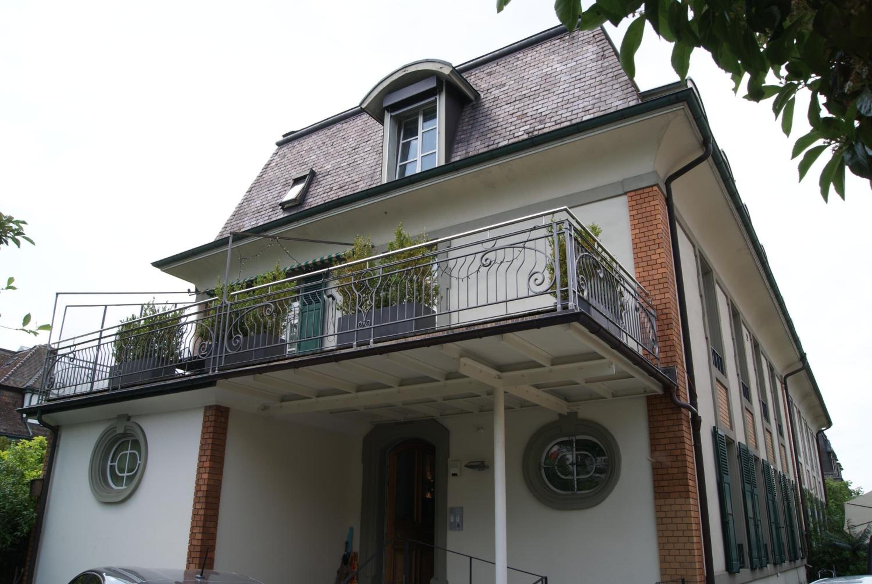A two-story building with a balcony, a window with shutters, and a door.