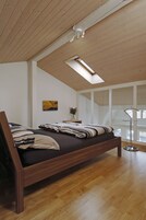 Quarto com cama de madeira, claraboia, pintura e vista para o exterior.