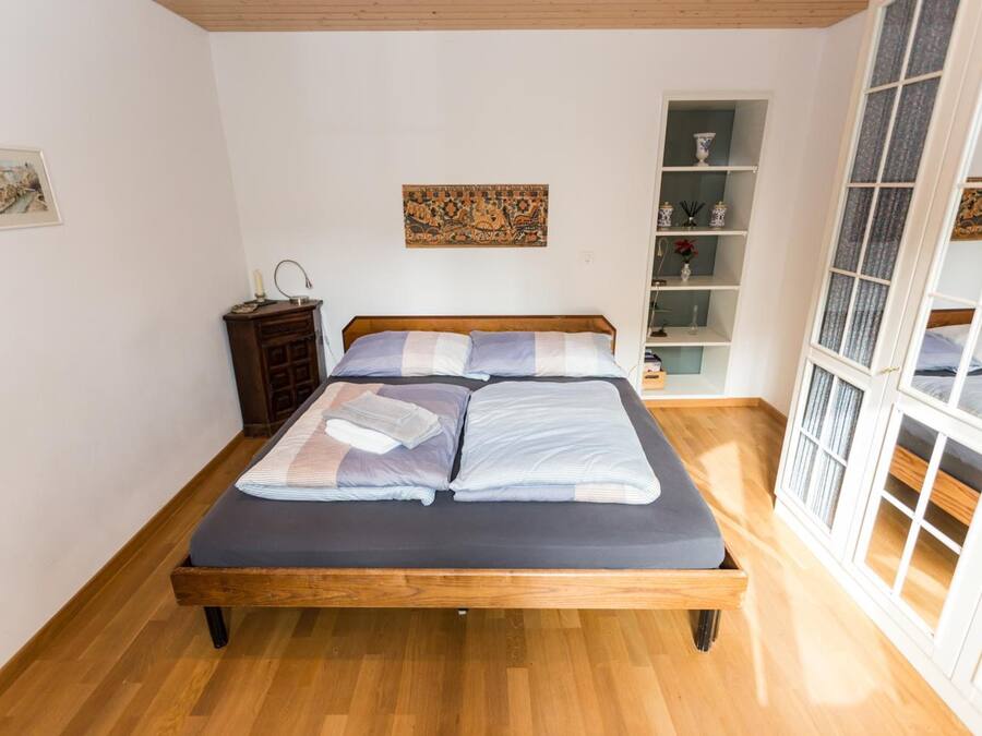 Une chambre à coucher avec un lit en bois, une table de chevet, une étagère avec des objets décoratifs et une fenêtre avec des rideaux.
