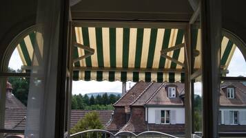 A balcony with a table and chairs, a striped awning, and a view of houses in the background.