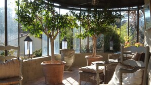 A covered patio with wicker furniture, potted trees, and a view of the surrounding area. - Les Rosées (Mougins)