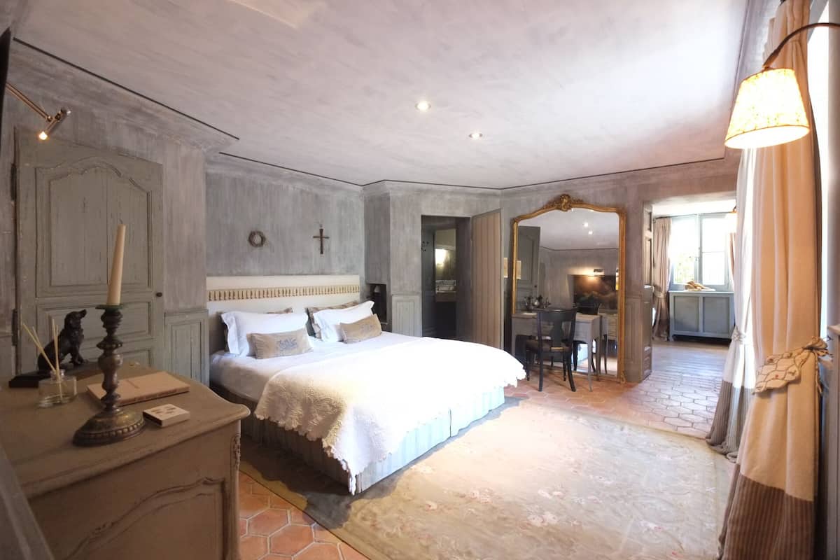 A bedroom with a large bed, a dresser, a mirror, and a window with curtains.