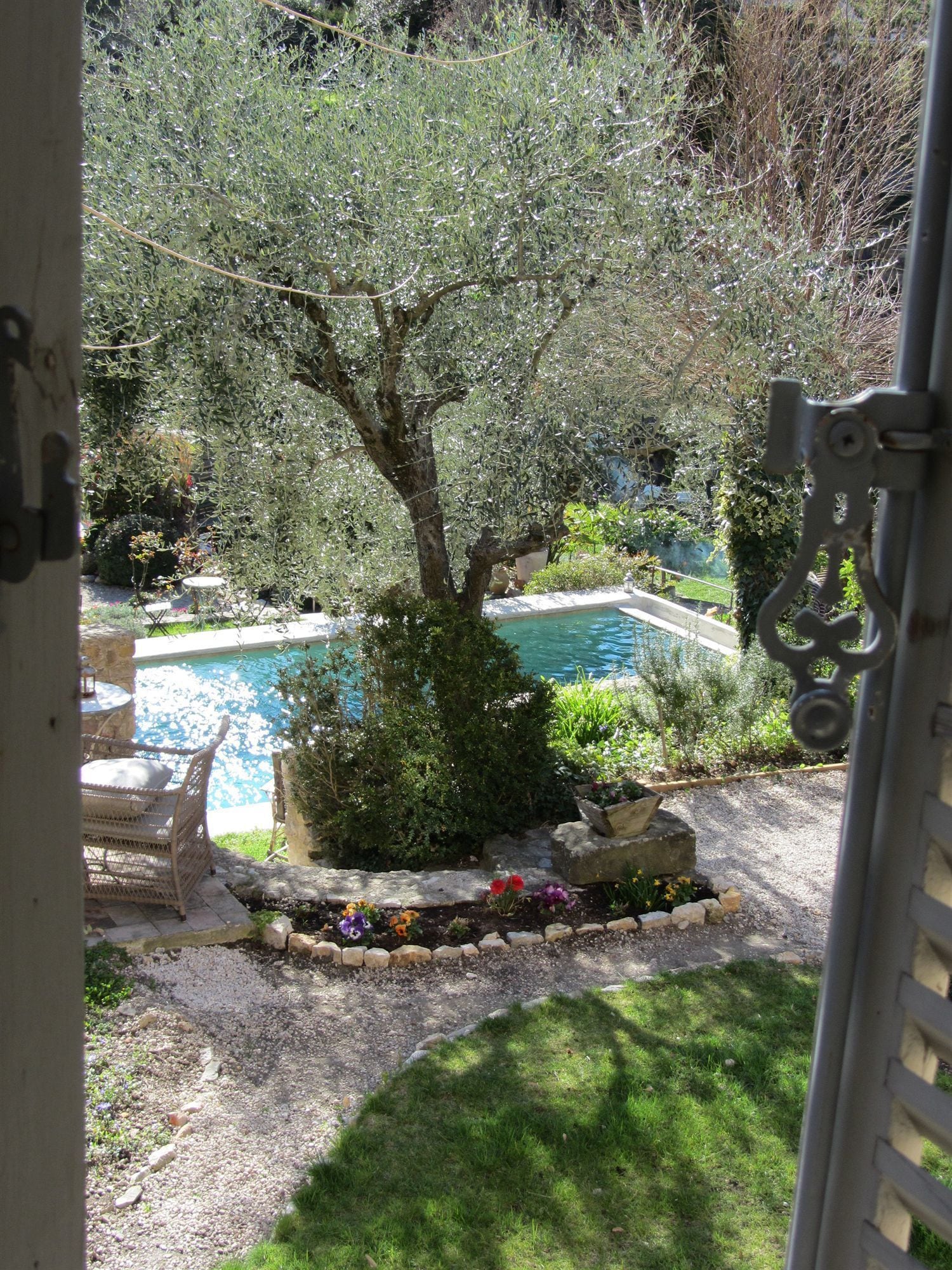 Une piscine entourée d’un jardin agrémenté d’un arbre, d’une chaise et d’un chemin en pierre.