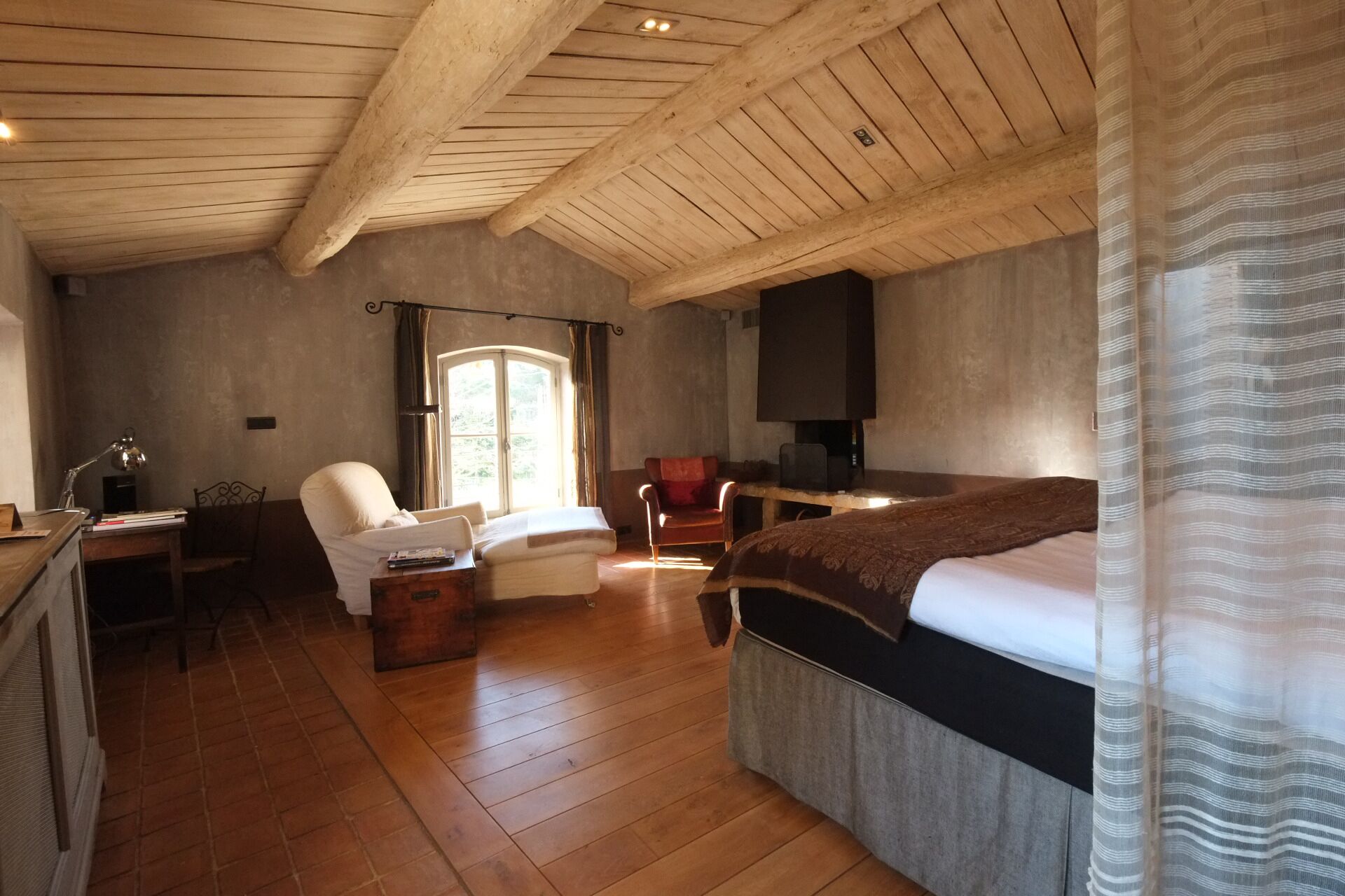 Een gezellige kamer met een houten plafond, een bed, een bureau en een stoel.