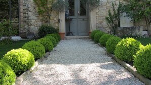 A stone building with a gravel pathway leading to a double door, surrounded by trimmed hedges. - Les Rosées (Mougins)