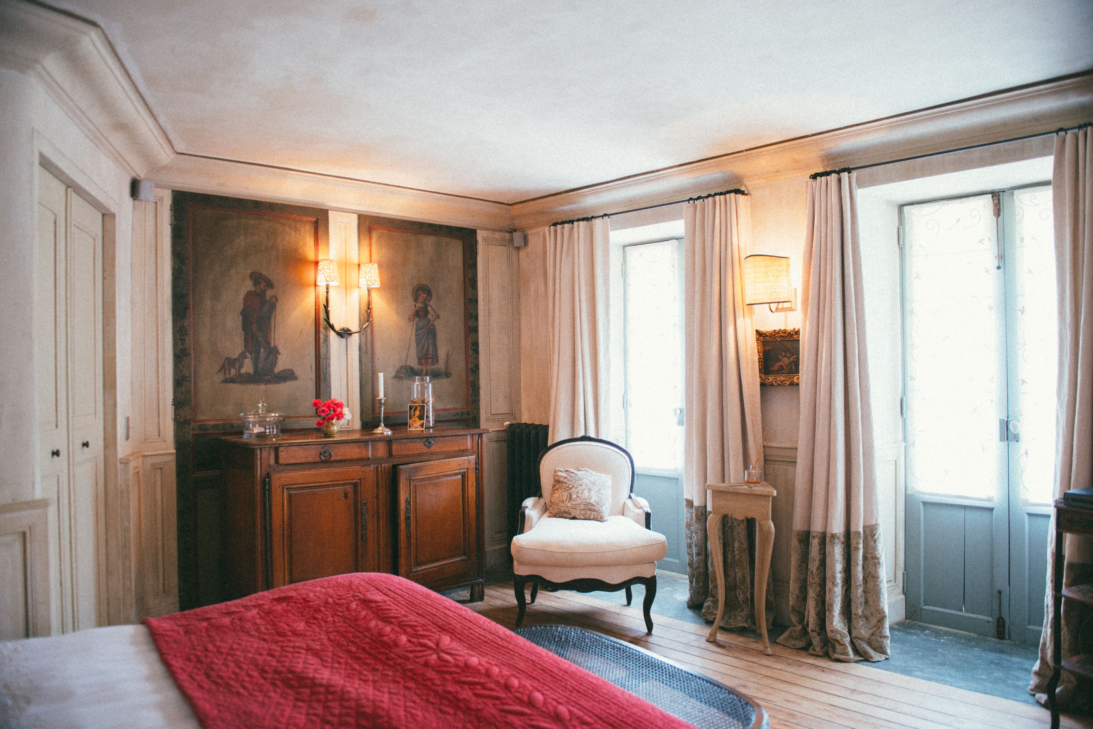 A hotel room with a bed, a chair, a small table, and a painting on the wall.