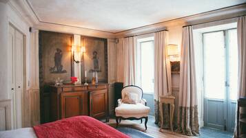 A hotel room with a bed, a chair, a small table, and a painting on the wall.