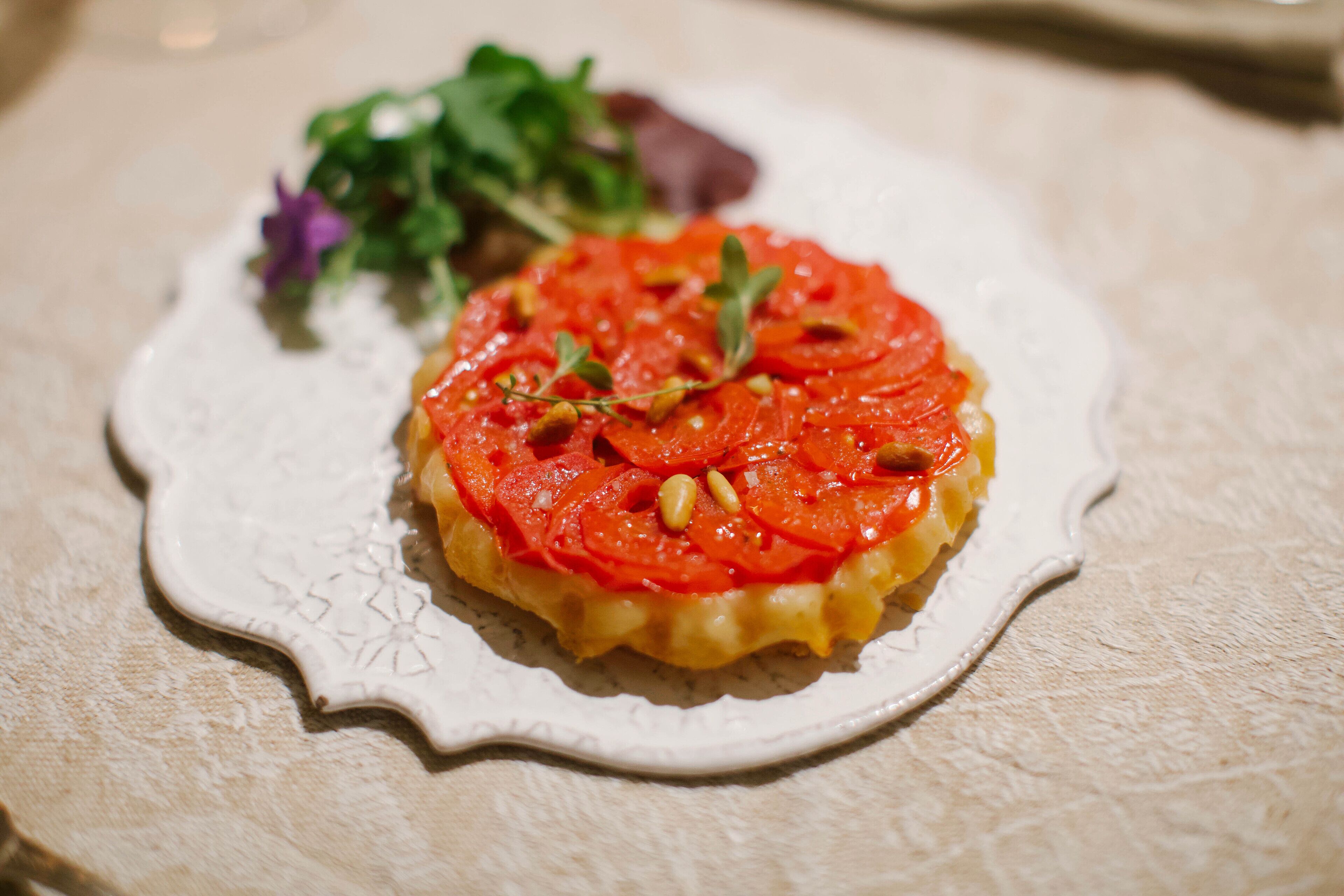 A plate with a tart topped with tomatoes and herbs, accompanied by a side salad.