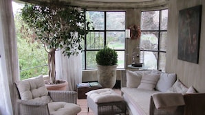 A cozy room with wicker furniture, a large potted plant, and a view of greenery outside. - Les Rosées (Mougins)