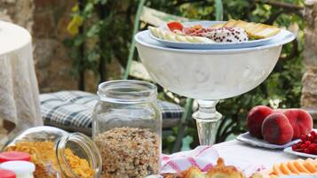 Una mesa al aire libre con diversas opciones de comida, incluyendo un cuenco de fruta, pasteles y frascos de conservas.