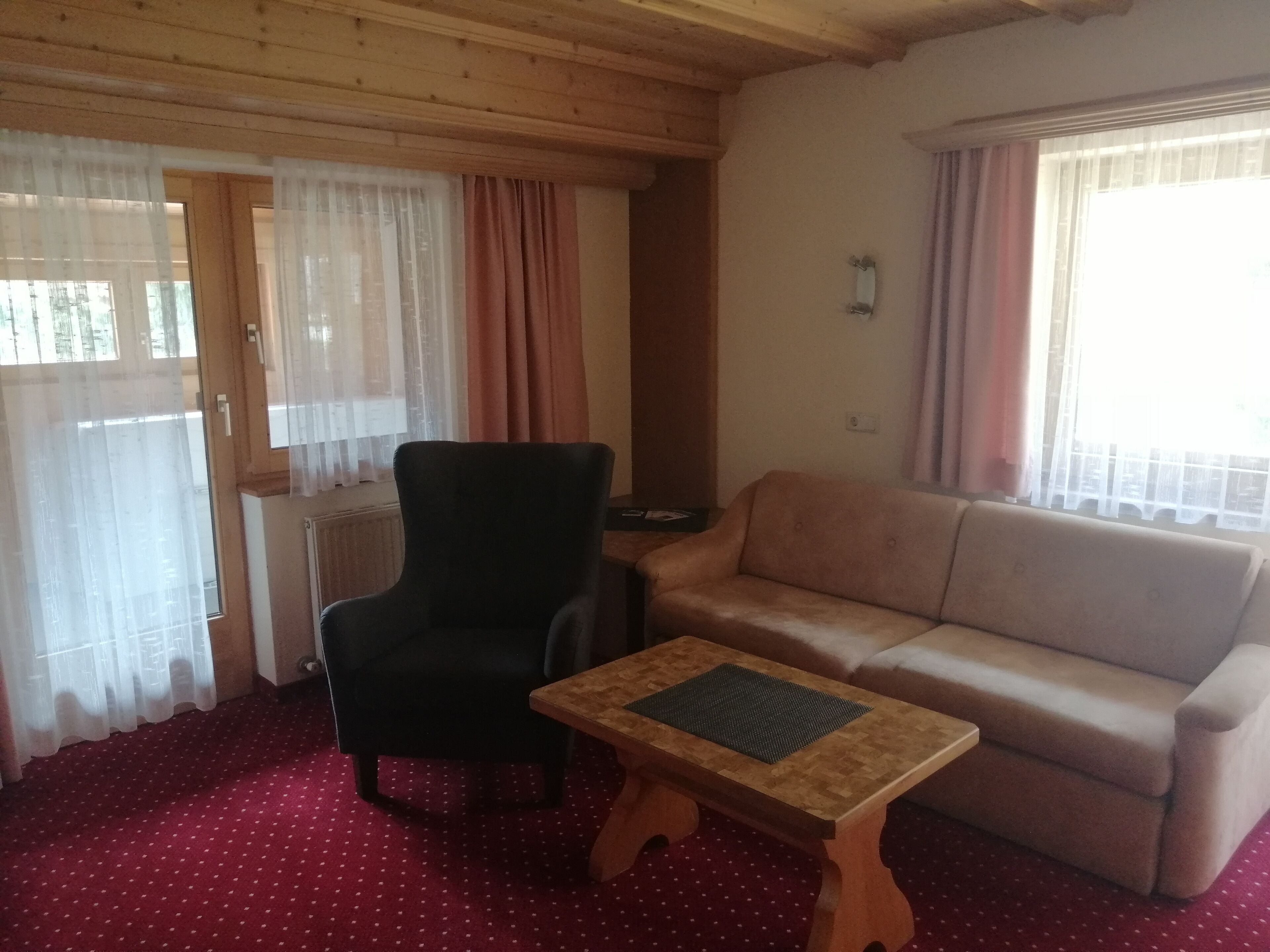 Een woonkamer met een zwarte fauteuil, een beige bank en een houten salontafel.