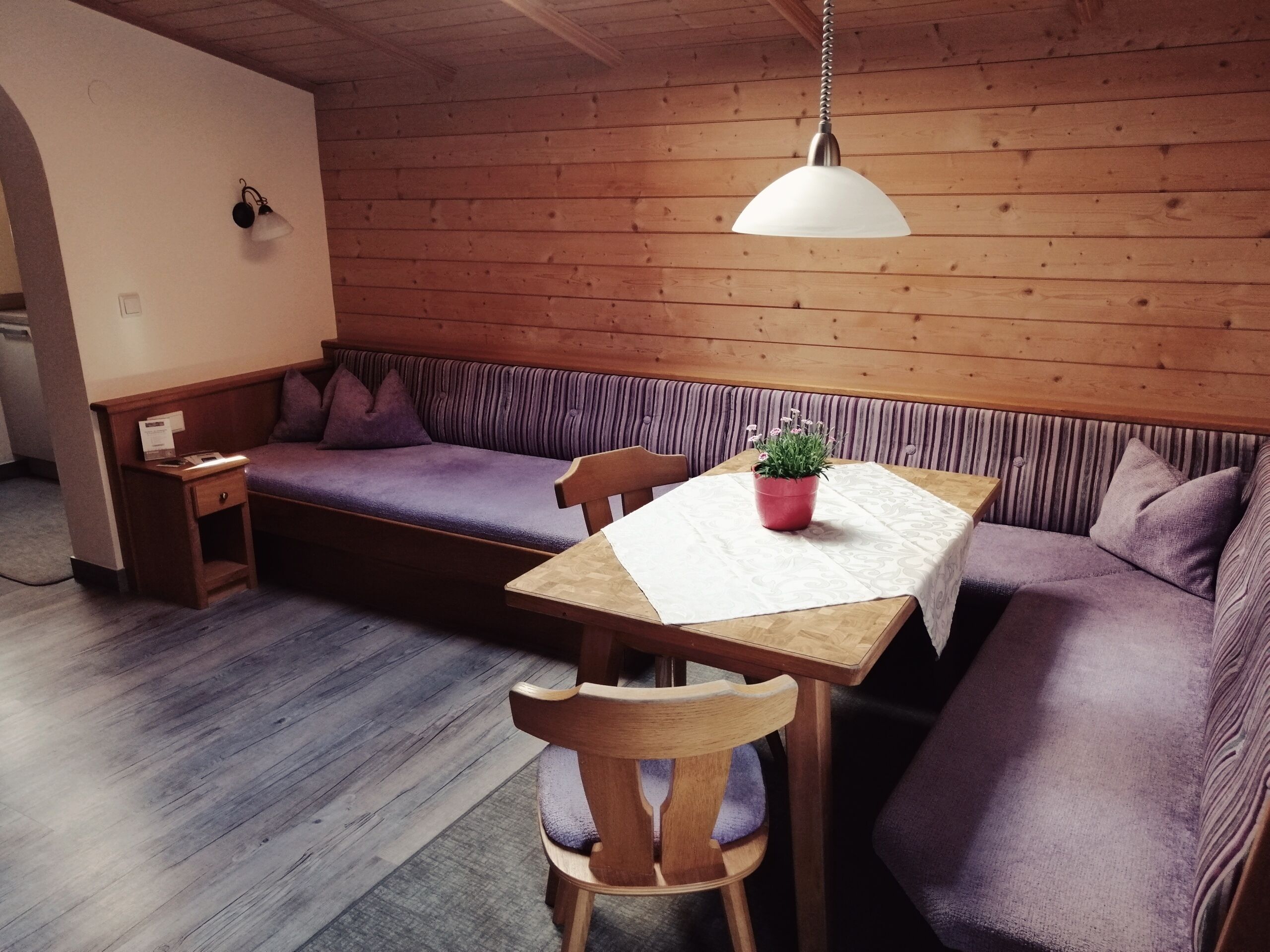 A cozy dining area with a wooden table, chairs, and a bench. A potted plant is on the table.