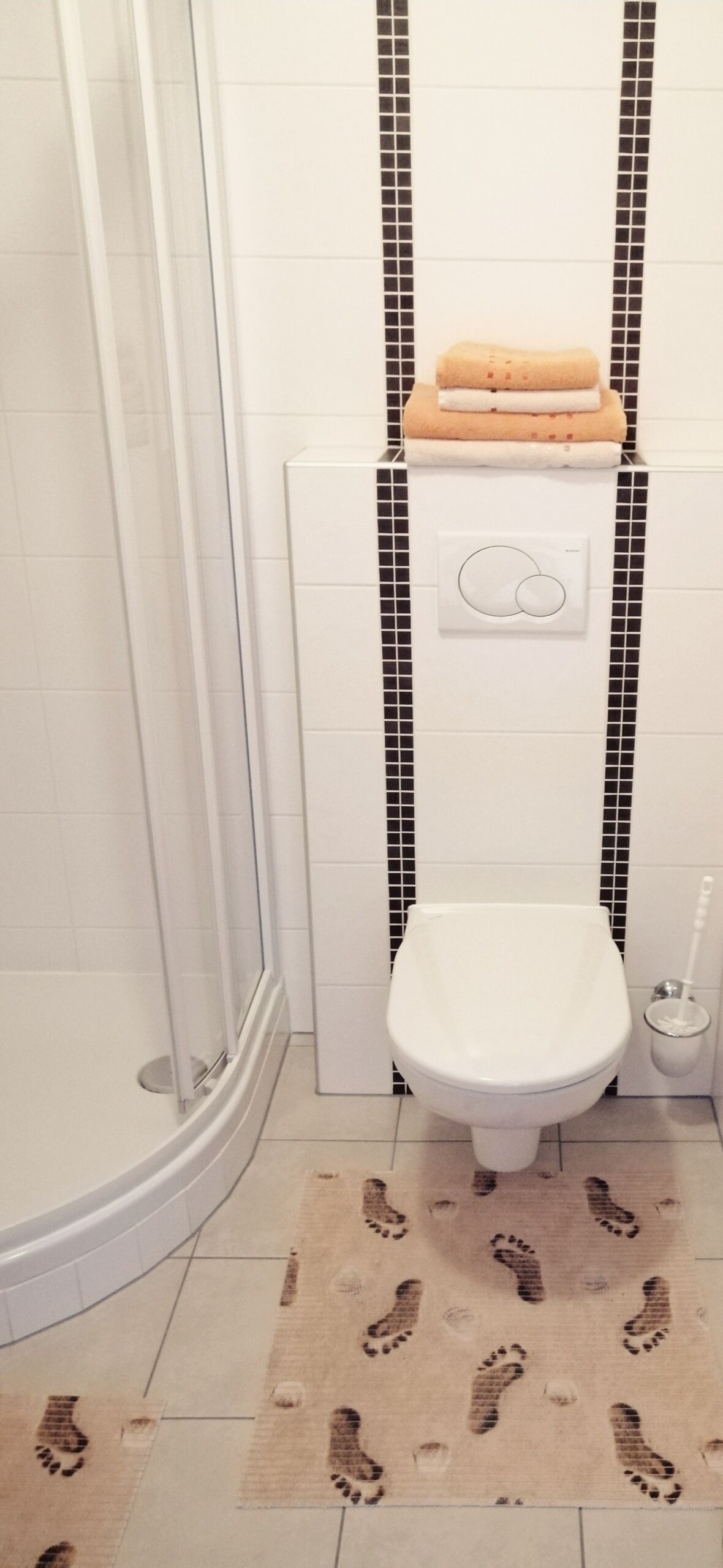 A bathroom with a shower, toilet, and a tiled floor with footprints.