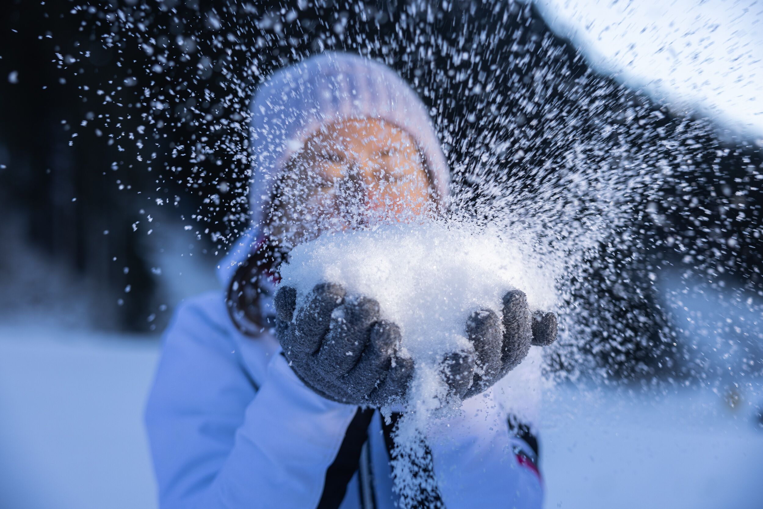 A person in a white coat and gloves interacting with snow.