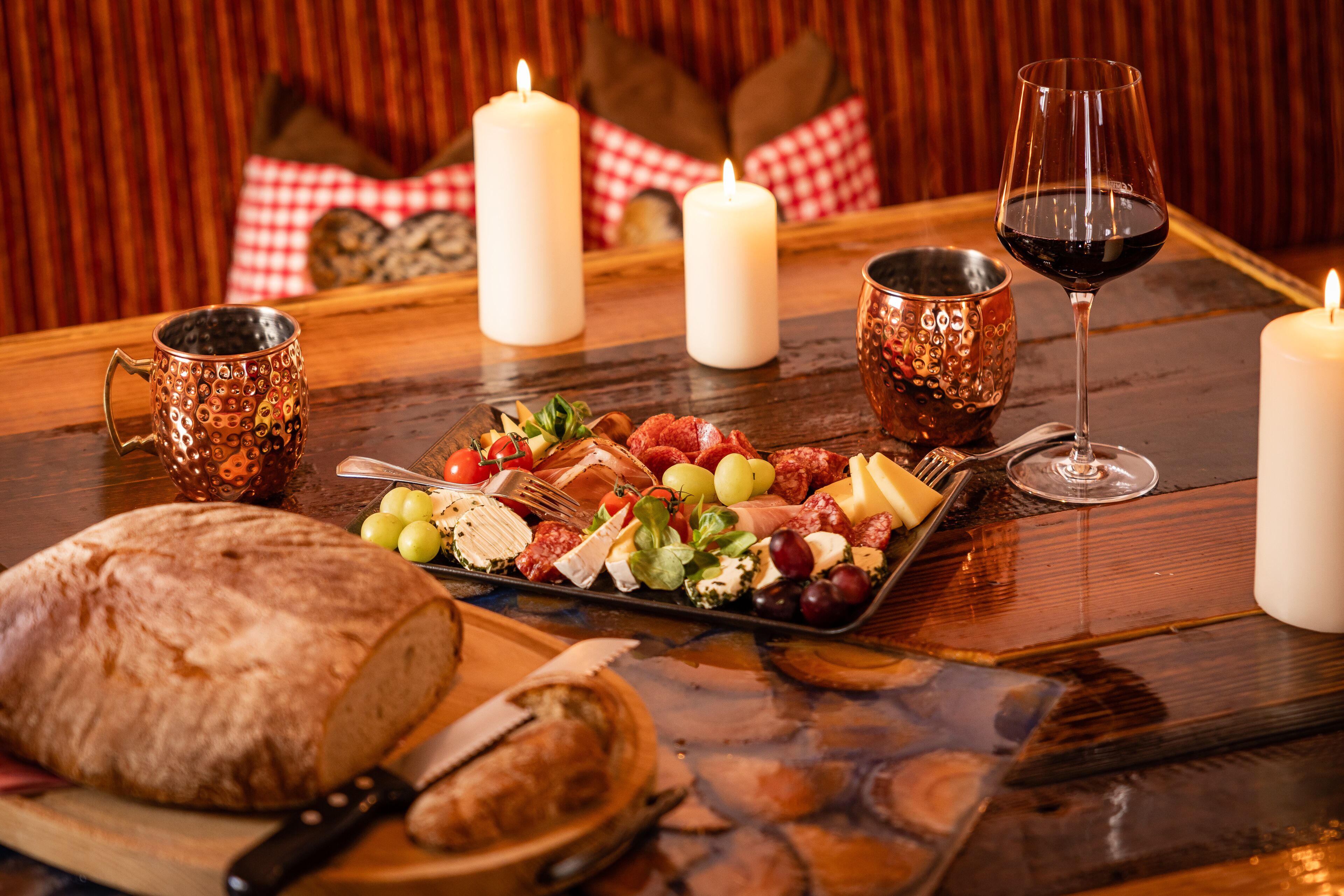 Une table en bois, sur laquelle on a disposé une planche de charcuterie, des bougies et un verre de vin rouge.
