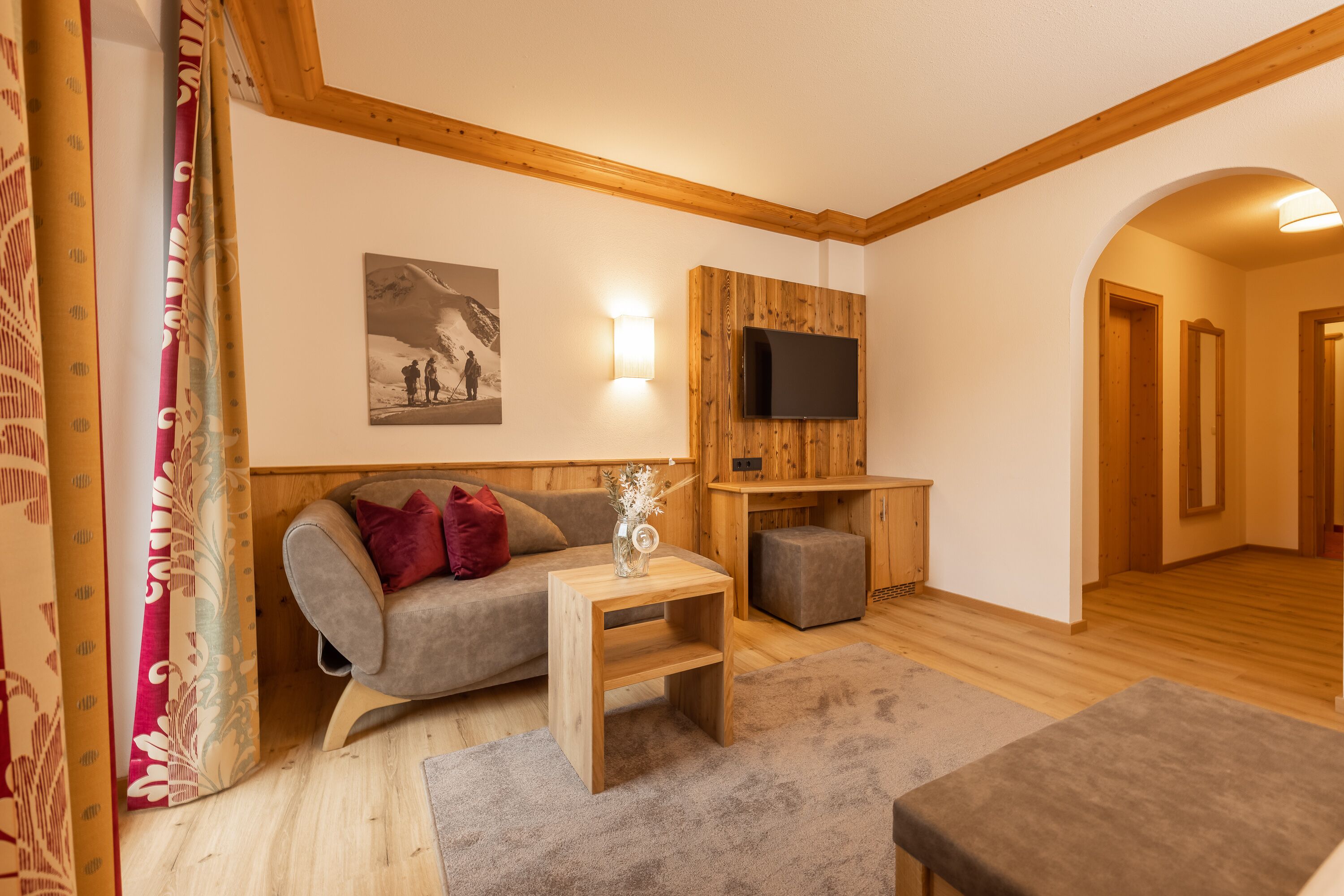 Un salón acogedor con un sofá gris, una mesita de madera, un televisor montado en un panel de madera y suelo de madera.