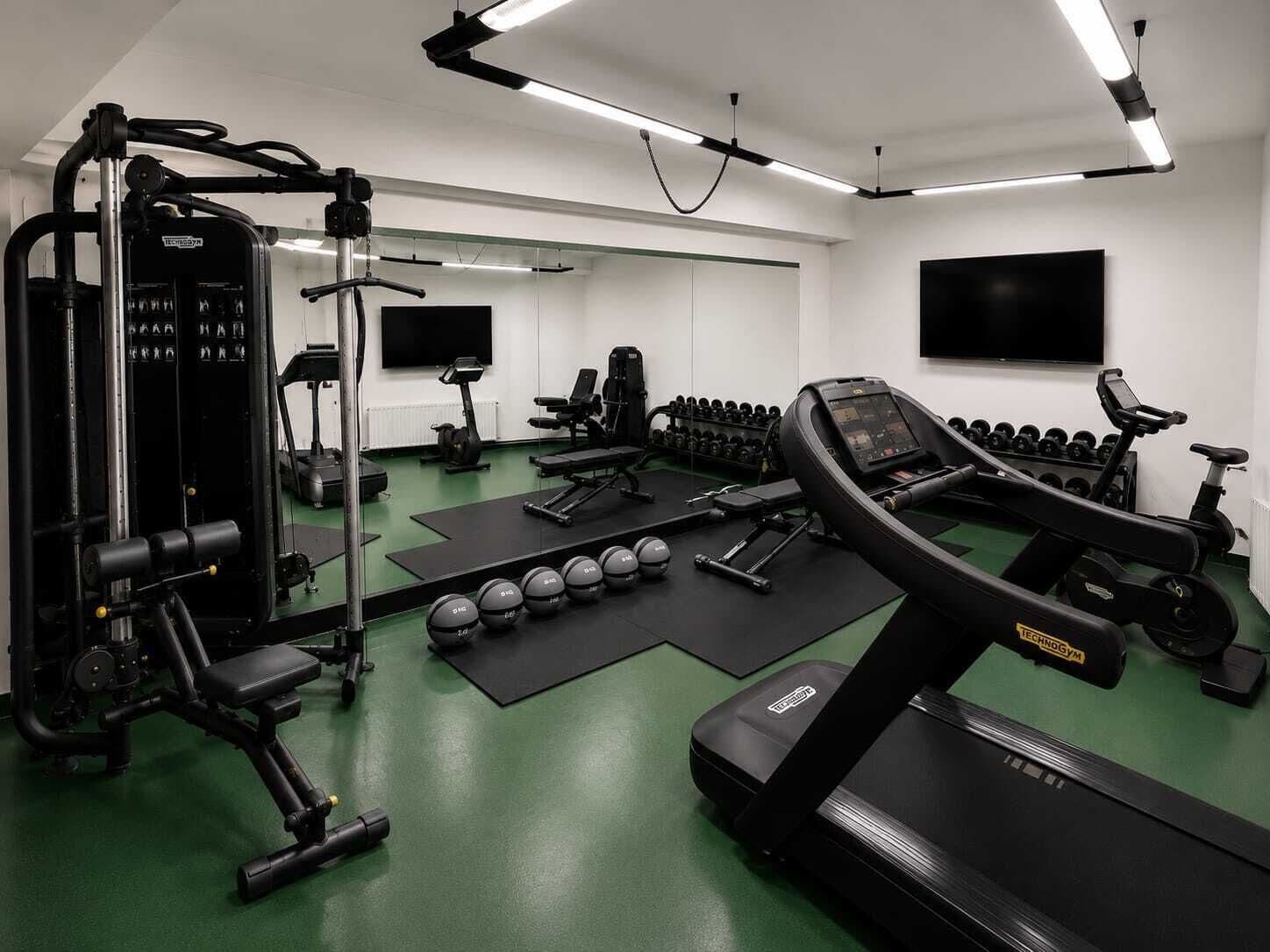 Een fitnessruimte met trainingsapparatuur, loopbanden en gewichten.