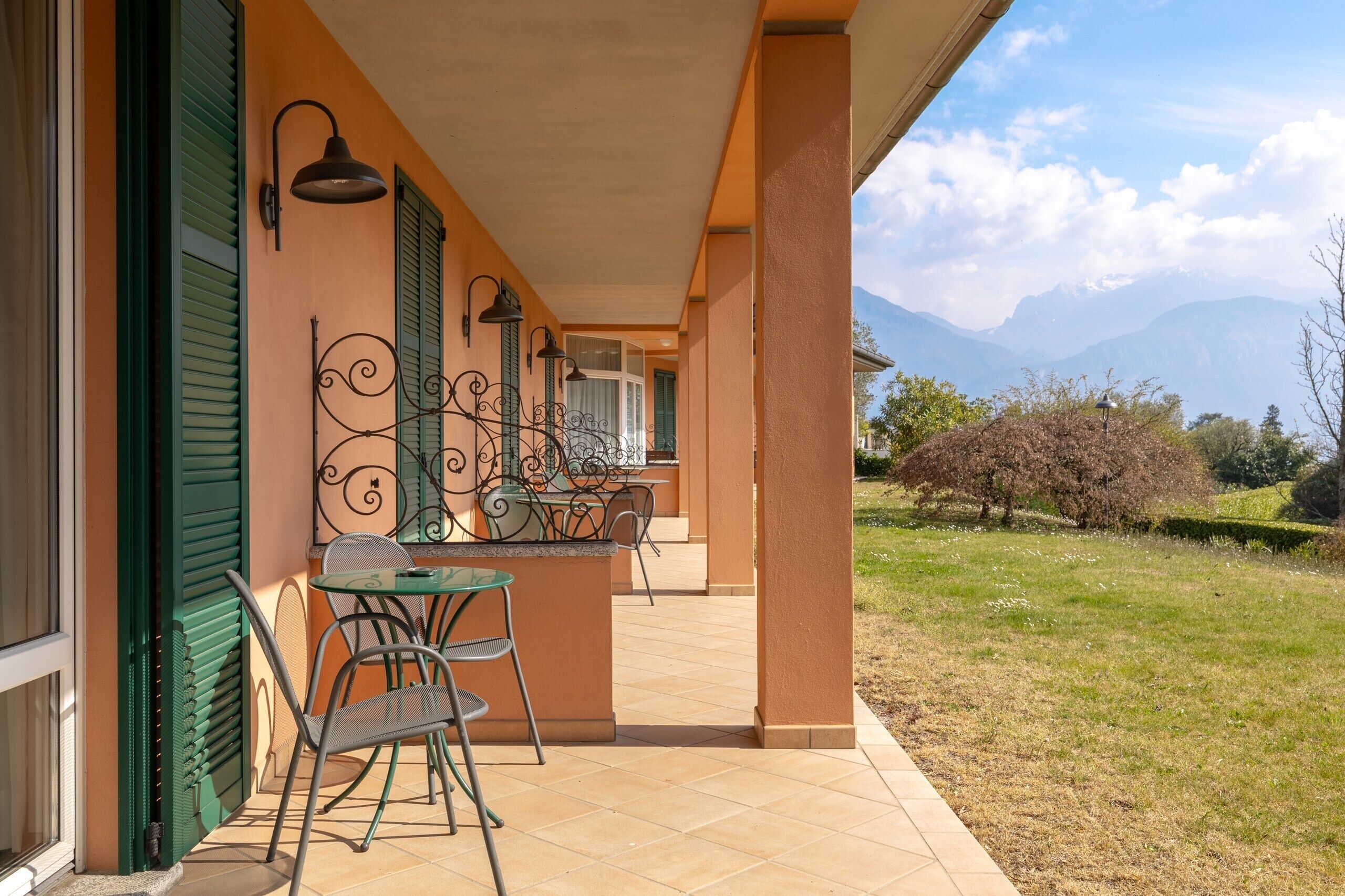 A patio with outdoor seating, a view of mountains, and a building with green shutters.